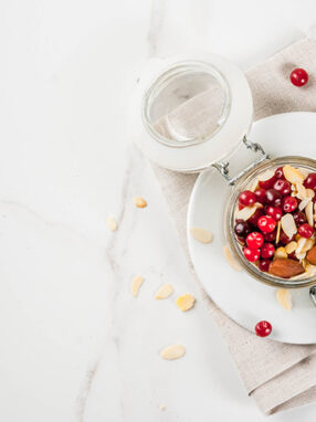 Recipe for a healthy winter breakfast, ideas for Christmas morning. Overnight oatmeal with almonds, cranberries, sugar. On a white marble table. copy space top view